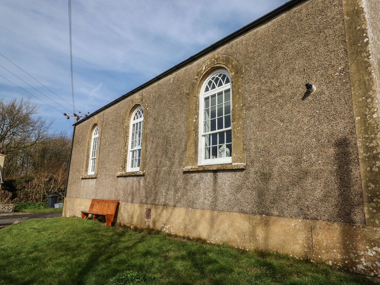 A building with three arched windows and a bench outside.