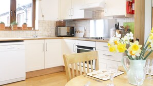 A modern kitchen with white cabinets, a microwave, a stove, and a dining area with a wooden table and chairs. - Acorn Cottage 1 (Shrewsbury)