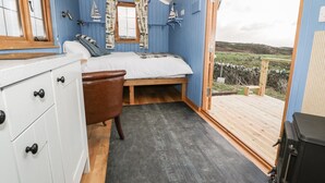 A cozy bedroom with a bed, a chair, and a view of the outdoors. - Cysgod y Bugail (Holyhead)