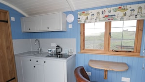 A compact kitchen with white cabinets, a sink, and a window with a view of the outdoors. - Cysgod y Bugail (Holyhead)