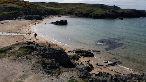 A coastal landscape with rocky terrain, a sandy beach, and calm water. - Cysgod y Bugail (Holyhead)