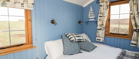 A bedroom with a bed, a window, a wall-mounted light, and a small shelf.