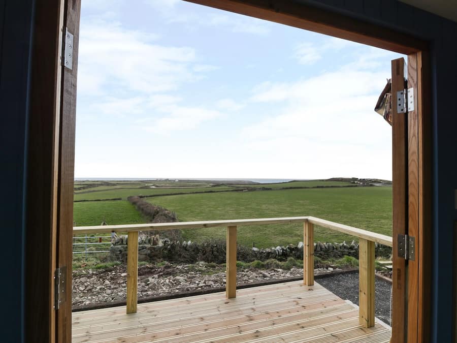 A wooden deck with a metal railing overlooking a green field and distant hills.