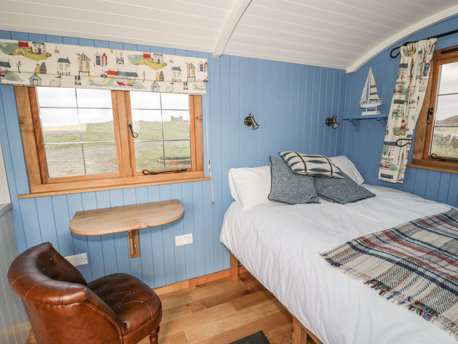 A bedroom with a bed, a wooden bench, a leather chair, and a window with a view of the outdoors.
