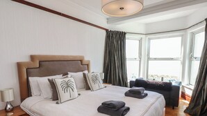 A hotel room with a large bed, a nightstand, a desk, and a view of the outdoors. - Wavecrest (Pwllheli)