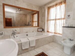 A bathroom with a large bathtub, a sink, a bidet, a mirror, and a window with curtains. - Wavecrest (Pwllheli)
