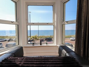 A room with a large bay window overlooking a beach, a sofa, and a small table with plants.