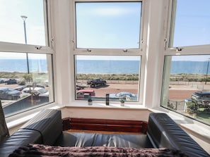 Habitación con un ventanal grande con vista a la playa, un sofá de cuero negro y una mesita con objetos decorativos.