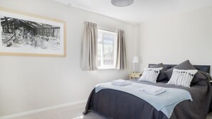 A bedroom with a large bed, a bedside table with a lamp, a window with curtains, and a framed picture on the wall. - Tai Candryll (Llanrwst)