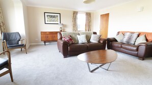 A living room with a brown leather sofa, a wooden coffee table, a wooden cabinet, and a framed picture on the wall. - Tai Candryll (Llanrwst)