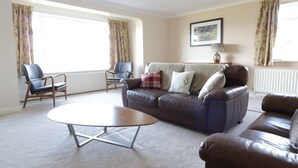 A living room with a brown leather sofa, two armchairs, a coffee table, and a lamp. - Tai Candryll (Llanrwst)