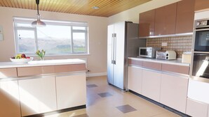 A modern kitchen with a large island, stainless steel appliances, and a view of the mountains through the window. - Tai Candryll (Llanrwst)