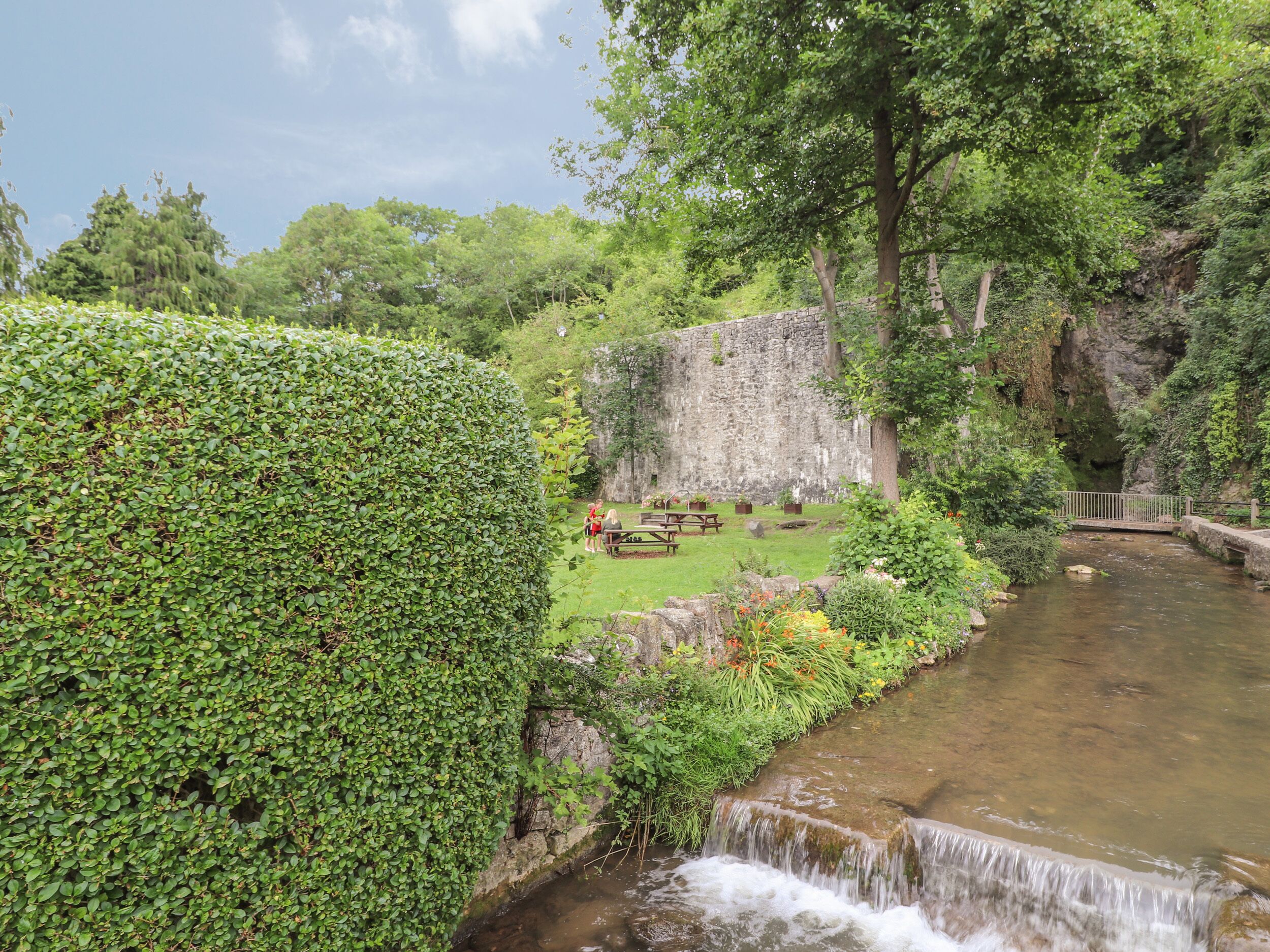 Un jardin paisible, avec un mur de pierre, une petite cascade et un espace aménagé pour pique-niquer.