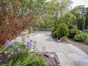 A paved pathway leading through a garden with various plants and shrubs. - Riverlea (Rhyl)