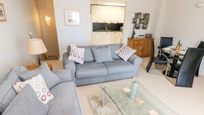A modern living room with a grey sofa, a glass coffee table, and a dining area with a glass table and black chairs. - 24 Rhodewood House (Saundersfoot)