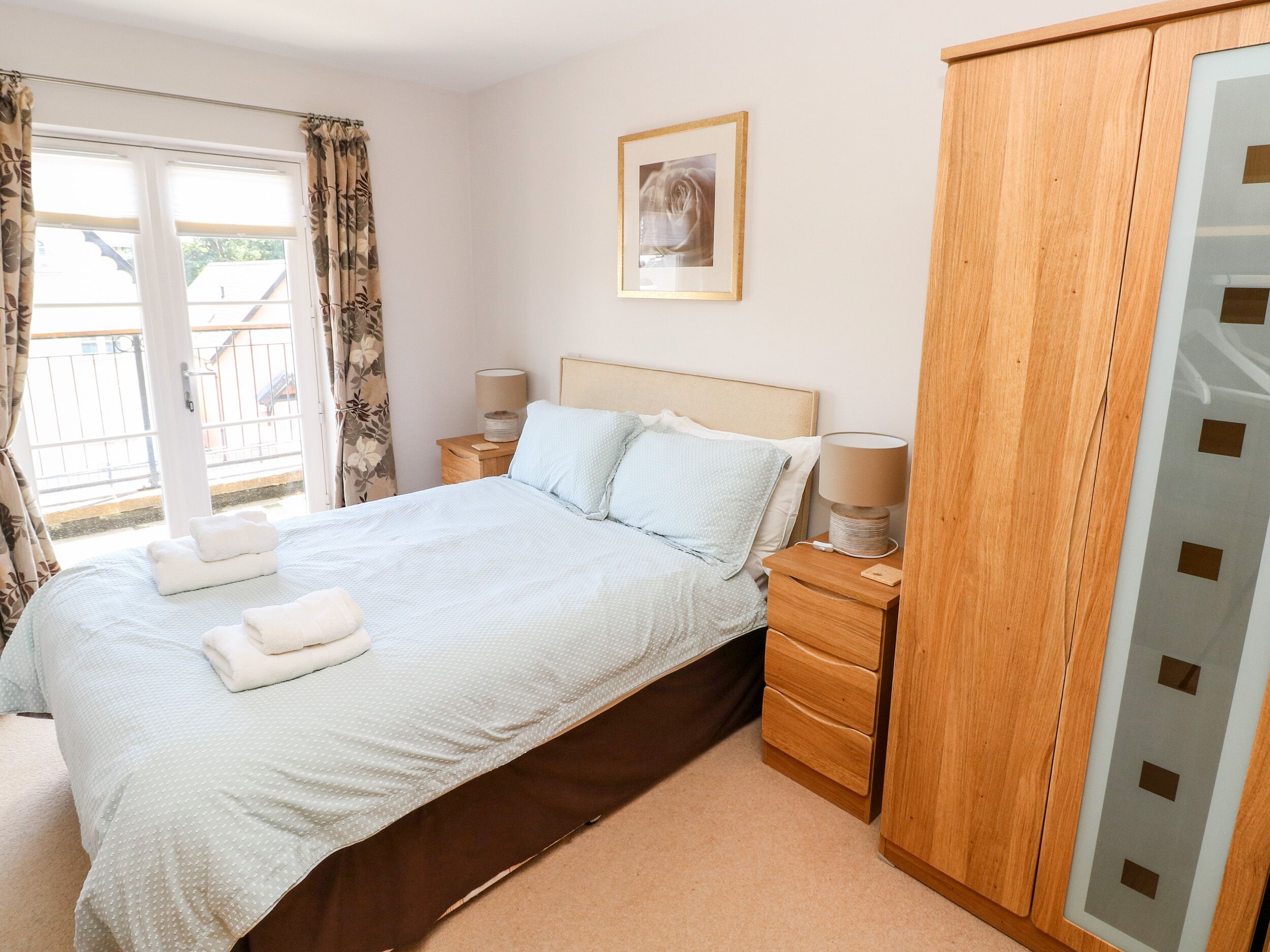 A bedroom with a bed, two bedside tables, a wardrobe, and a window with curtains.