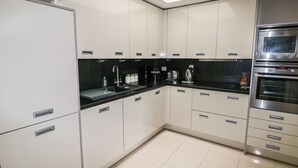 A modern kitchen with white cabinets, black countertops, and stainless steel appliances including a refrigerator, oven, and microwave. - 24 Rhodewood House (Saundersfoot)