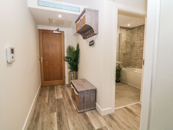A hallway with a wooden door, a small bench, a potted plant, and a bathroom visible through an open door. - 6 Bay View (Tyn-y-Gongl)
