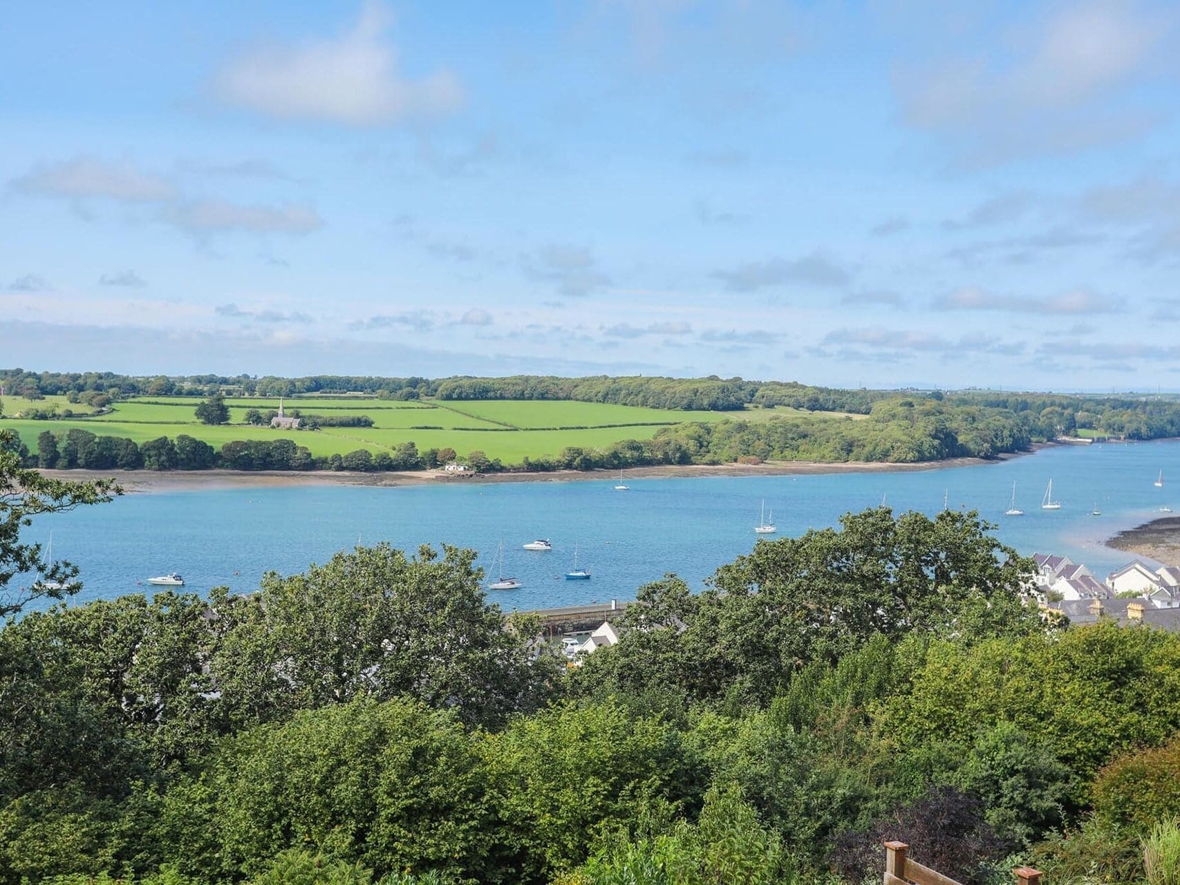 A coastal landscape with a view of a bay, boats, and greenery.