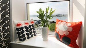 A window seat with a view of a body of water, a plant in a white vase, and two decorative pillows. - Glan Y Don (Y Felinheli)