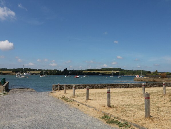 A coastal view with boats on the water, a stone wall, and a grassy area with wooden posts. - Glan Y Don (Y Felinheli)