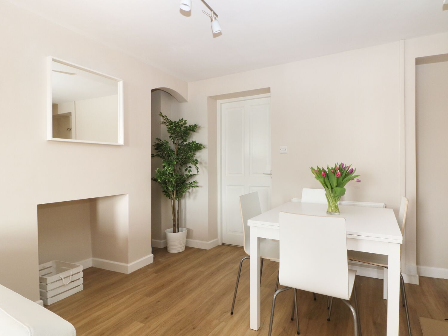 Un comedor moderno y minimalista con una mesa y sillas blancas, una planta en maceta y un jarrón con flores.