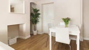 A modern, minimalist dining area with a white table and chairs, a potted plant, and a vase with flowers. - Glan Y Don (Y Felinheli)