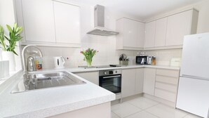 A modern kitchen with white cabinetry, a stainless steel sink, a built-in oven, and a microwave. - Glan Y Don (Y Felinheli)