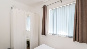 A hotel room with a bed, a window with curtains, a wardrobe, and a trash bin. - Sea Breeze (Burnham-on-Sea)