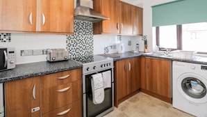 A modern kitchen with wooden cabinets, a built-in oven, a microwave, a toaster, and a washing machine. - Sea Breeze (Burnham-on-Sea)