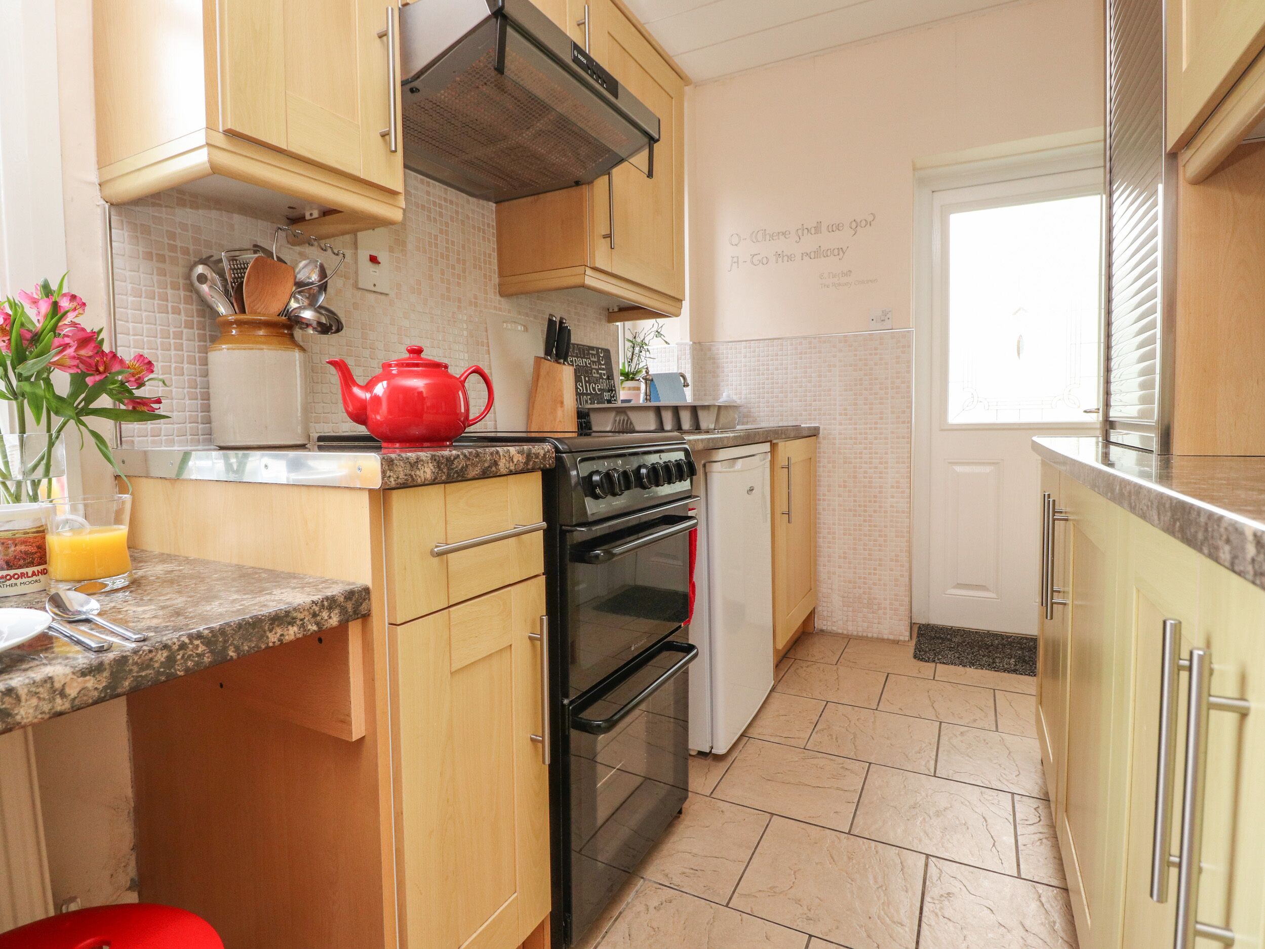 A kitchen with wooden cabinets, a red teapot, a stove, and a dishwasher.
