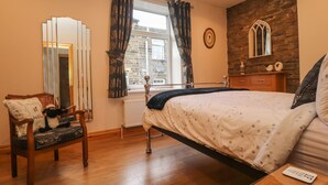 A bedroom with a bed, a chair, a dresser, a mirror, and a window with curtains. - Heather Corner (Keighley)