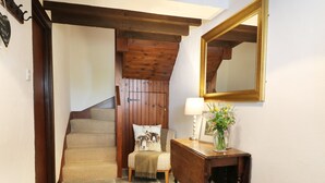 A staircase with wooden beams, a console table with a lamp and flowers, and a mirror on the wall. - The Hayloft (Grange-over-Sands)