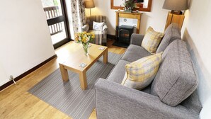 A cozy living room with a sofa, a wooden coffee table, a fireplace, and a large mirror. - The Hayloft (Grange-over-Sands)