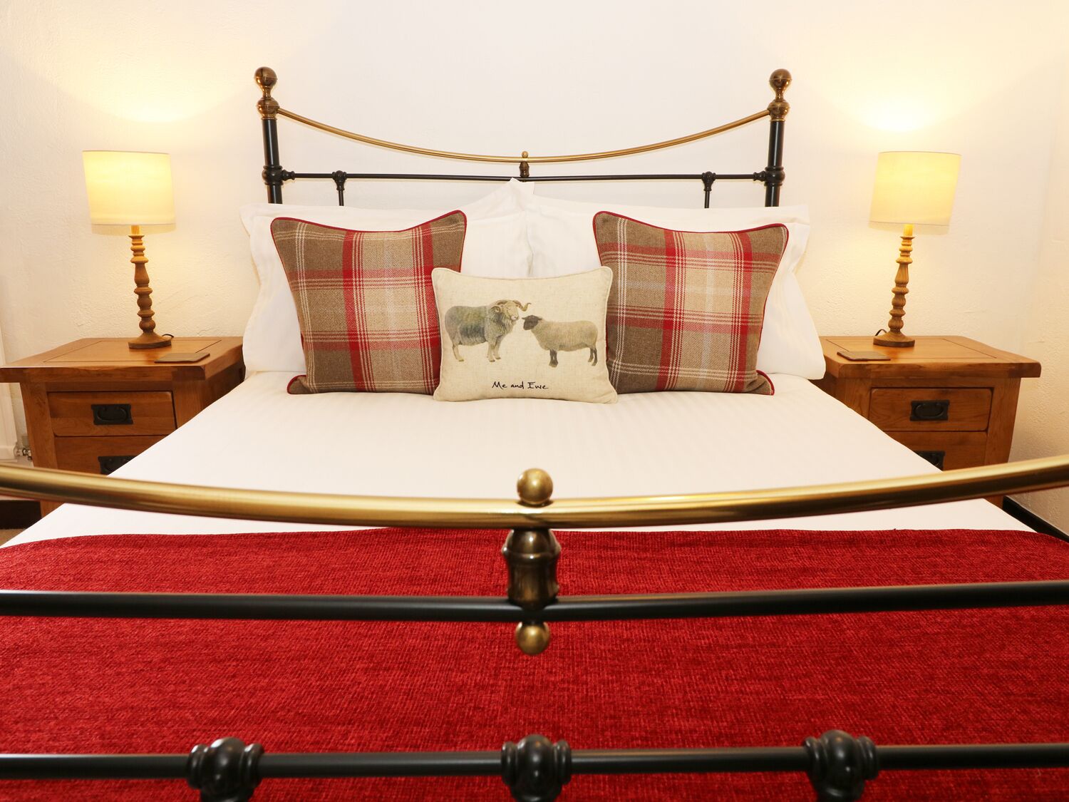 A bed with a red throw blanket, two nightstands with lamps, and a headboard with a gold finish.