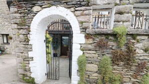 A stone building with a white archway entrance, a metal gate, and a stone wall with greenery. - The Hayloft (Grange-over-Sands)
