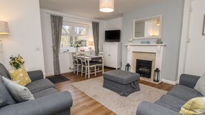 A living room with grey sofas, a dining table, a fireplace, and a TV. - Rose Cottage (Alnwick)