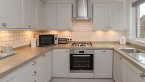 A compact kitchen with white cabinets, a microwave, toaster, stove, oven, and a sink. - Rose Cottage (Alnwick)