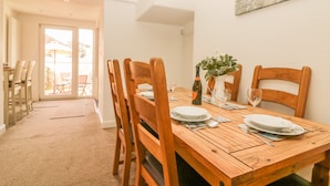 Un coin repas avec une table en bois dressée pour quatre personnes, des chaises, un vase avec des fleurs et une bouteille de vin.