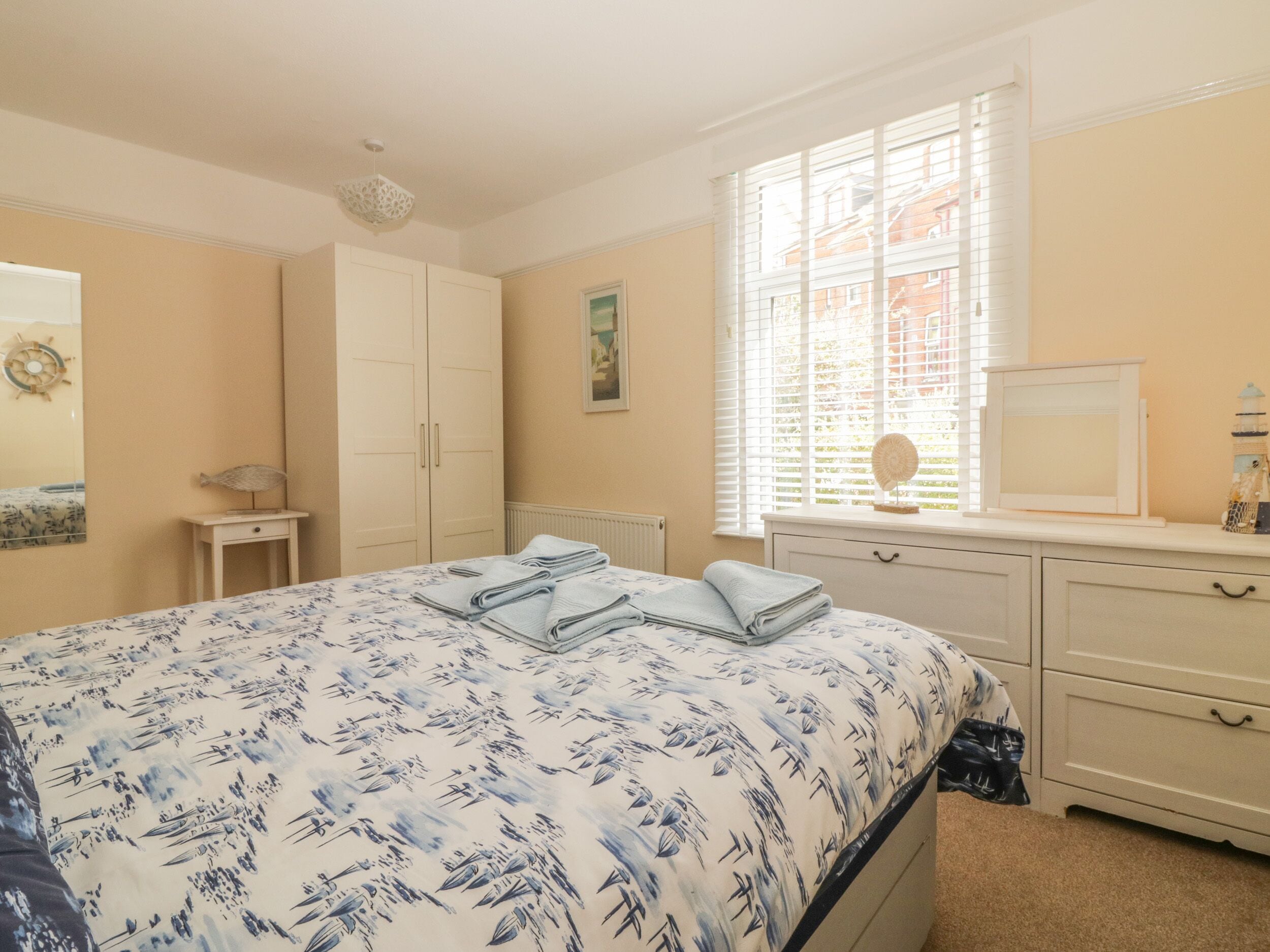 Een slaapkamer met een bed, een dressoir, een raam met zonwering en een radiator.