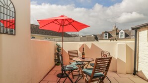 Une terrasse avec une table et des chaises, un parasol rouge et une bouteille de vin.