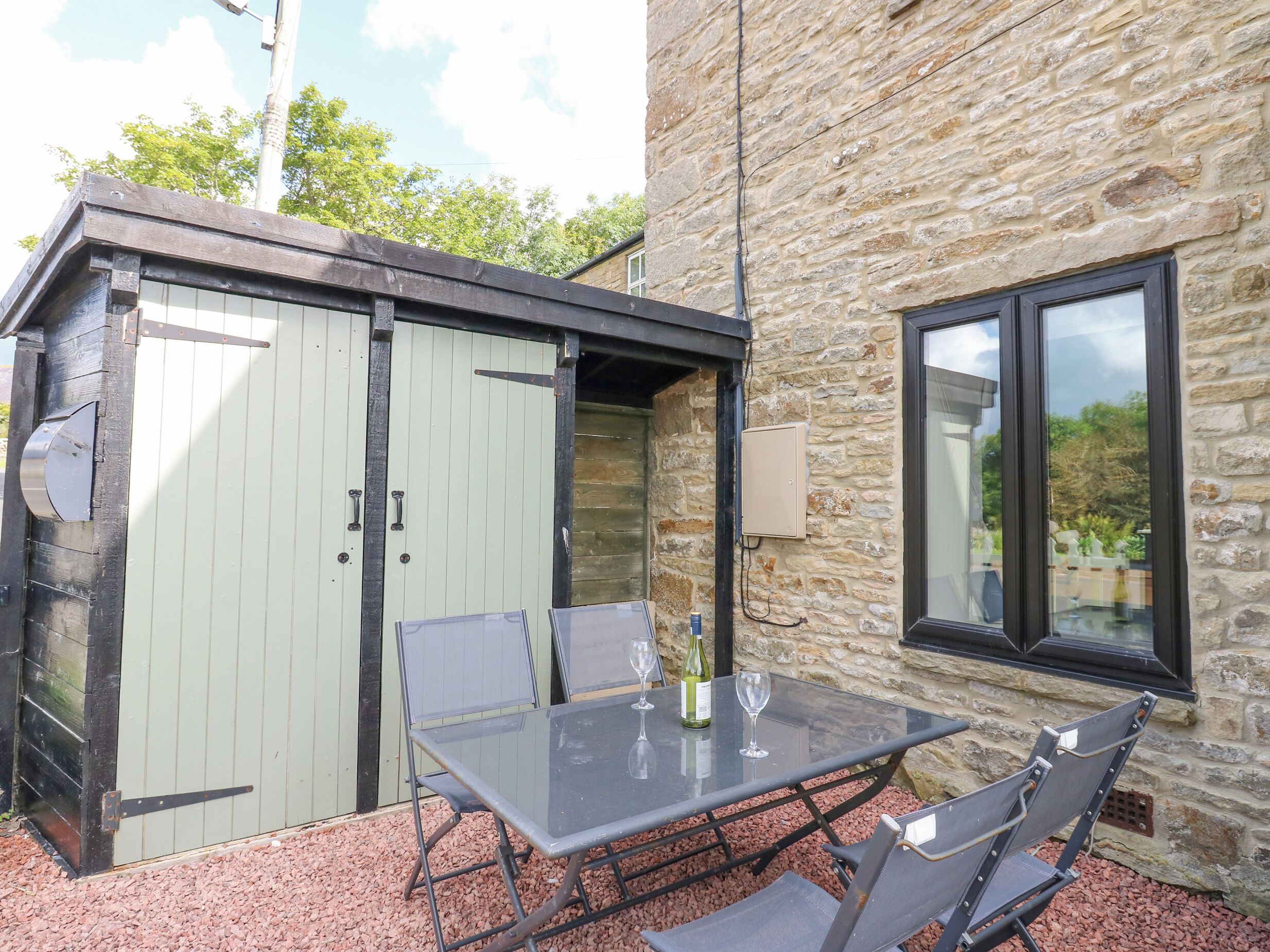 A stone building with a glass door and windows, a table with chairs, and a bottle of wine.