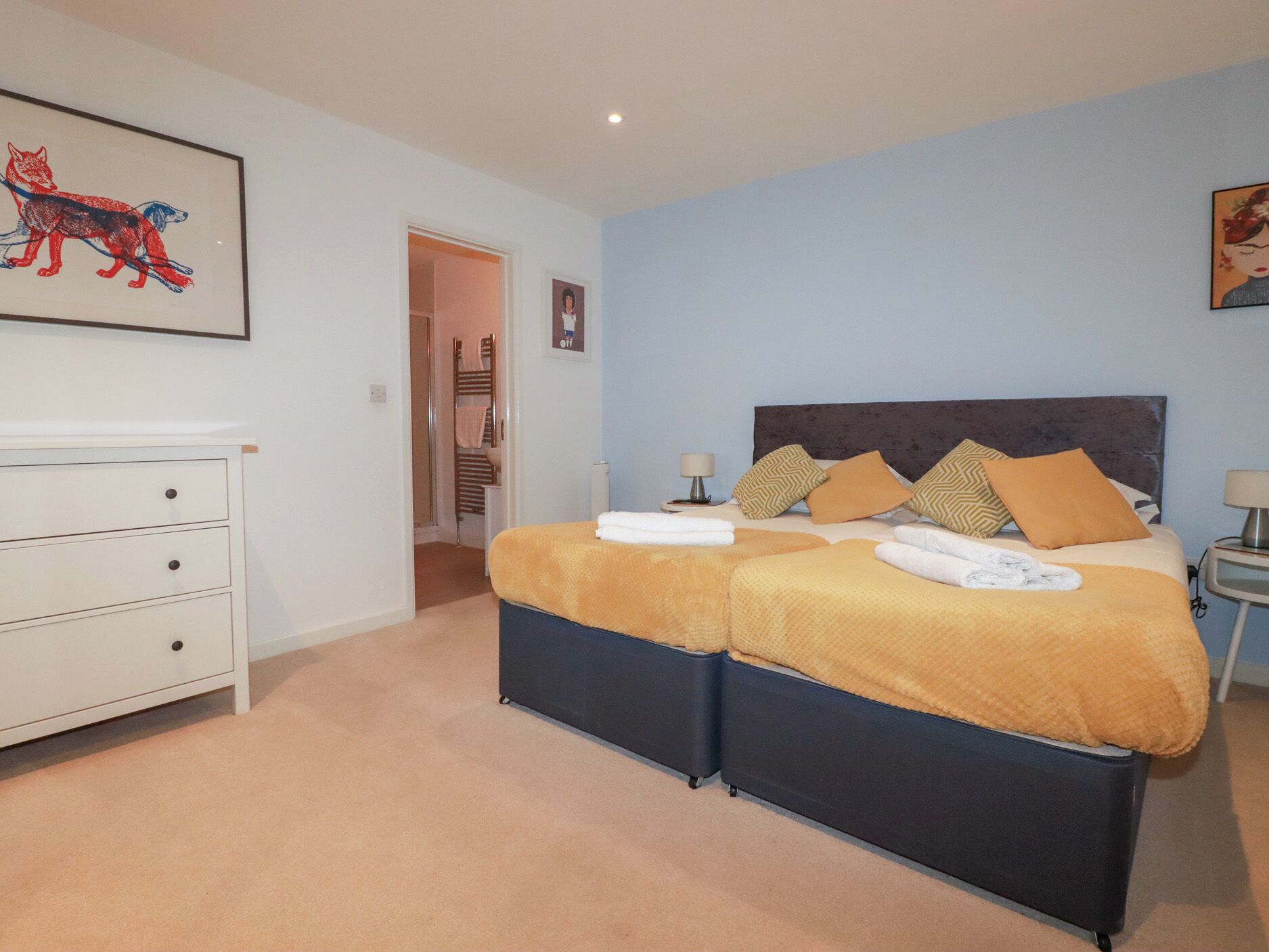 A bedroom with a double bed, two bedside tables, a white dresser, and a framed picture on the wall.