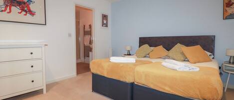 A bedroom with a double bed, two bedside tables, a white dresser, and a framed picture on the wall.
