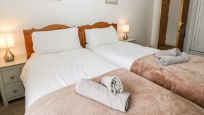 A double bed with white linens and a wooden headboard, two bedside tables with lamps, and a door to the right. - Spire View (Pickering)