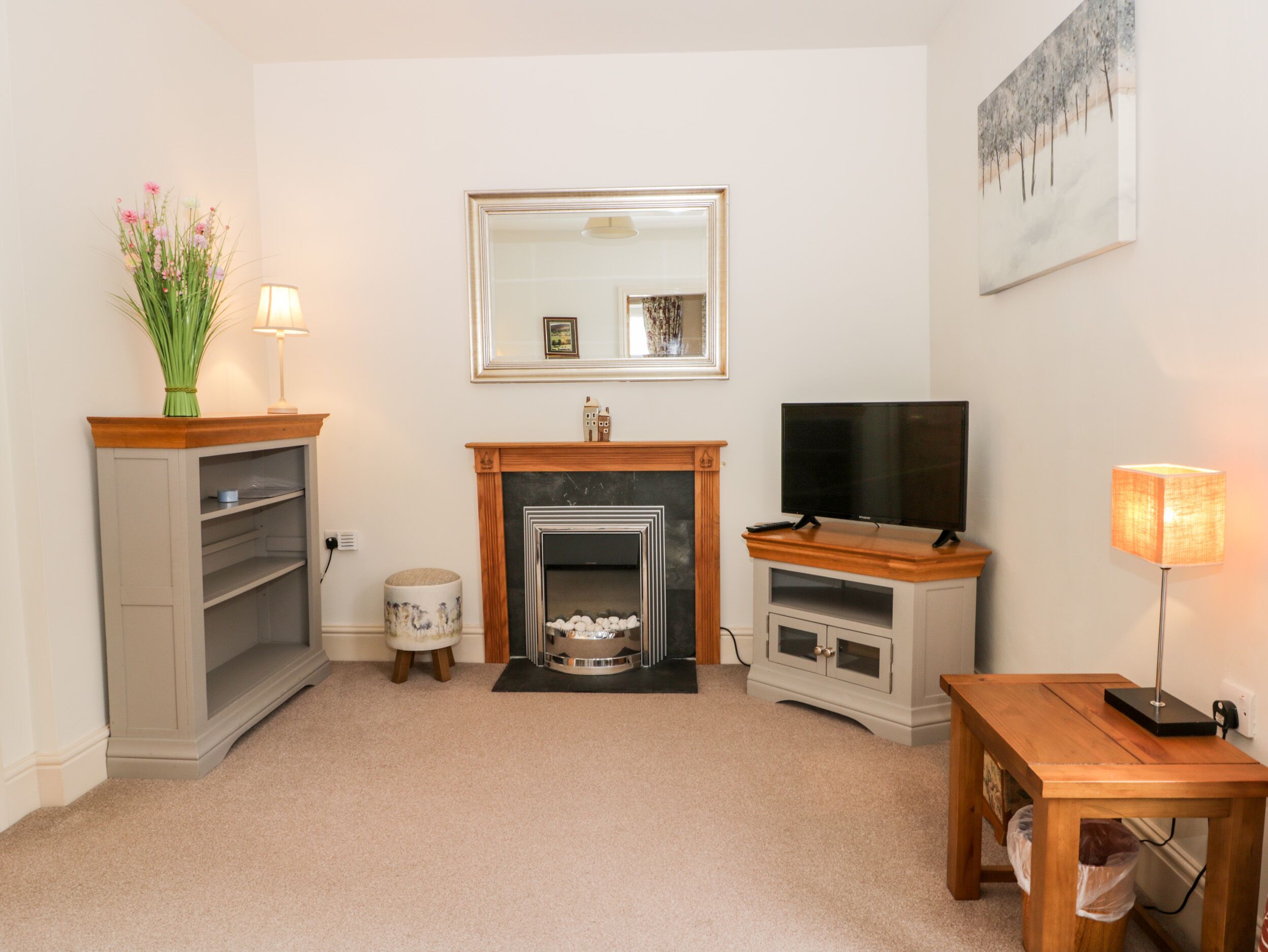 A living room with a fireplace, television, and a table with a lamp.