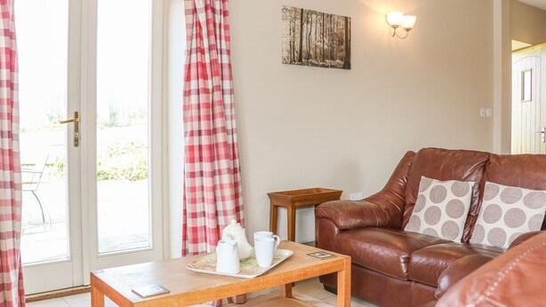 A cozy living room with a brown leather sofa, a wooden coffee table with a tray of white mugs, and a painting on the wall. - The Old Dairy (Worthing)