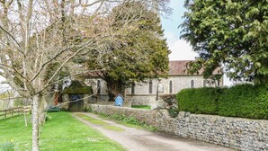 A stone building with a traditional architectural style, a paved pathway leading to it, and a well-maintained hedge. - The Old Dairy (Worthing)