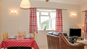 A dining area with a table set for two, a sofa, a TV, and a window with curtains. - The Old Dairy (Worthing)