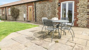 A patio area with a table and chairs, a stone wall, and a door. - The Old Dairy (Worthing)
